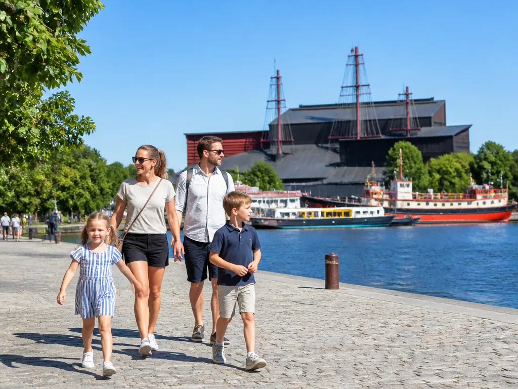 Barnfamilj promenerar längs vattnet vid Vasamuseet på Djurgården en solig sommardag