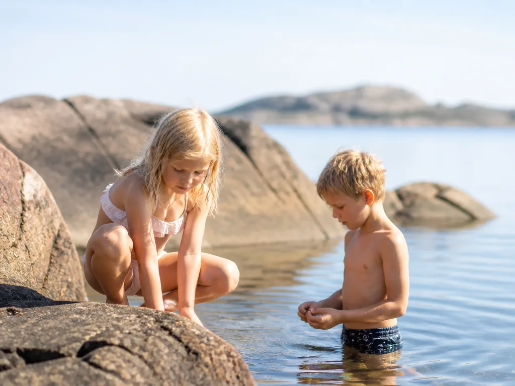 Barn leker på klipporna längs en svensk skärgårdsstrand en solig sommardag